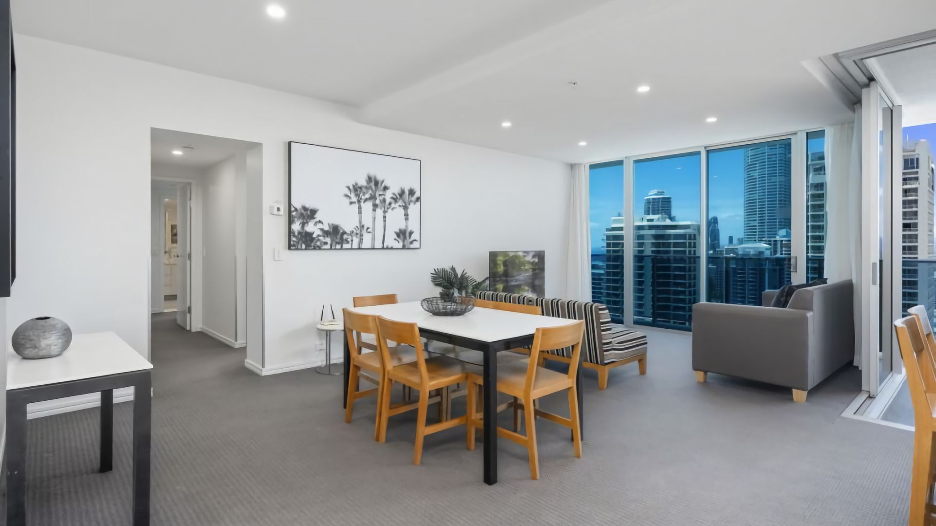 A modern dining area with a table and chairs, a sofa, and a large window with a city view.