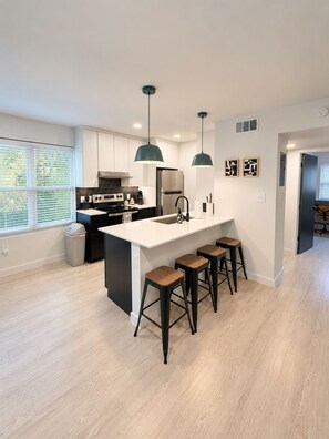 A modern kitchen with a central island, bar stools, and pendant lighting. - Modern 2BR | Near Downtown Austin & SoCo (Austin)
