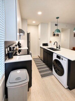 A compact kitchen with a washing machine, a coffee machine, and a trash bin. - Modern 2BR | Near Downtown Austin & SoCo (Austin)