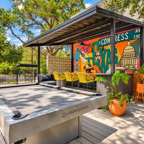 An outdoor pool area with a mural, yellow chairs, and a concrete table. - Modern 2BR | Near Downtown Austin & SoCo (Austin)
