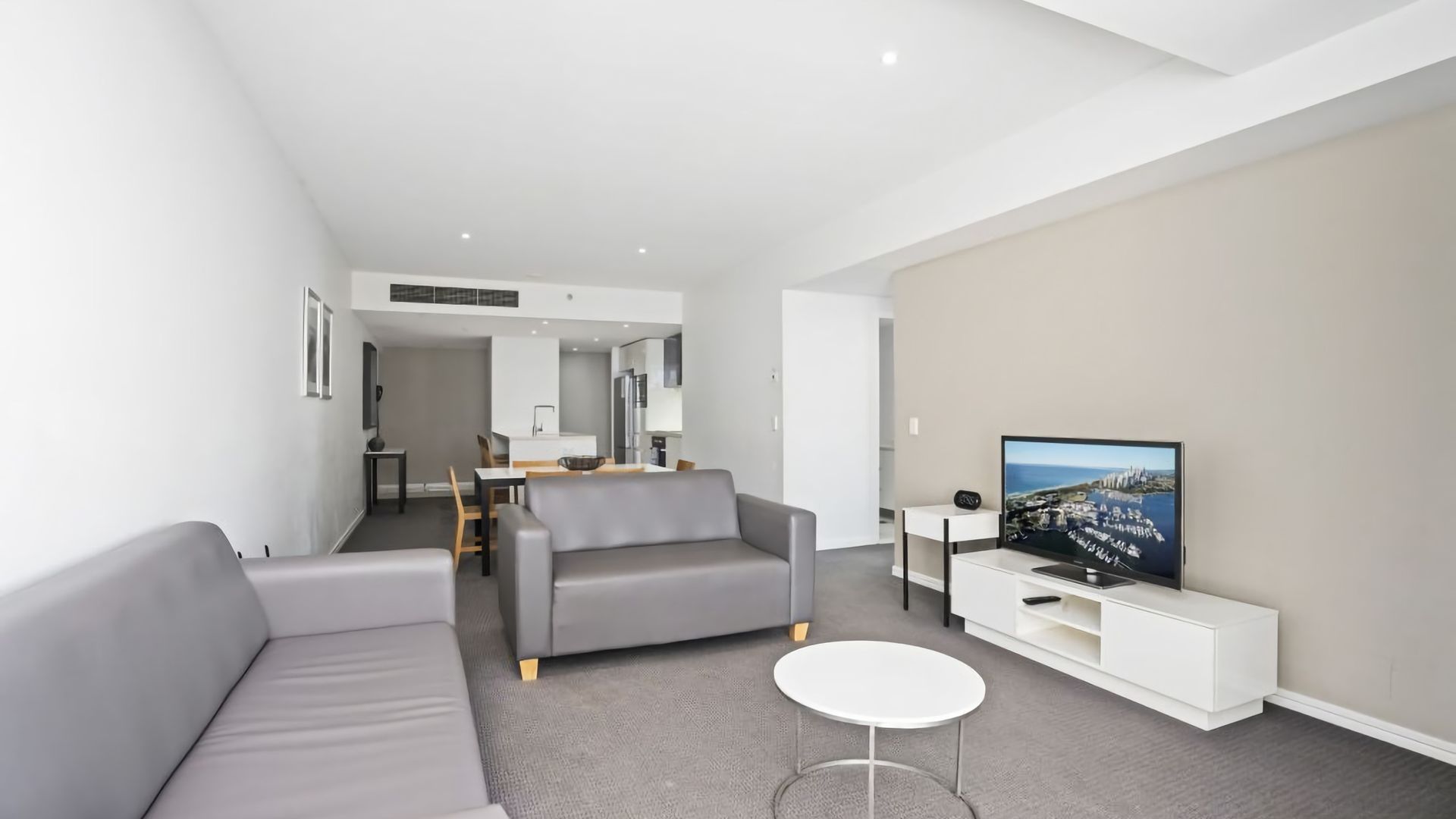 A modern living room with a grey sofa, a small white table, and a flat-screen TV on a white stand.