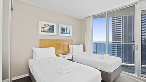 Ett hotellrum med två sängar, ett nattduksbord, en lampa och utsikt över staden.