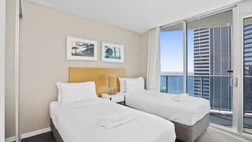 A hotel room with two beds, a nightstand, a lamp, and a view of the city.