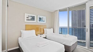 A hotel room with two beds, a nightstand, a lamp, and a view of the city. - Orchid Residences Apartment 22603 (Surfers Paradise)
