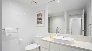 A modern bathroom with a toilet, sink, and mirror. - Orchid Residences Apartment 22603 (Surfers Paradise)