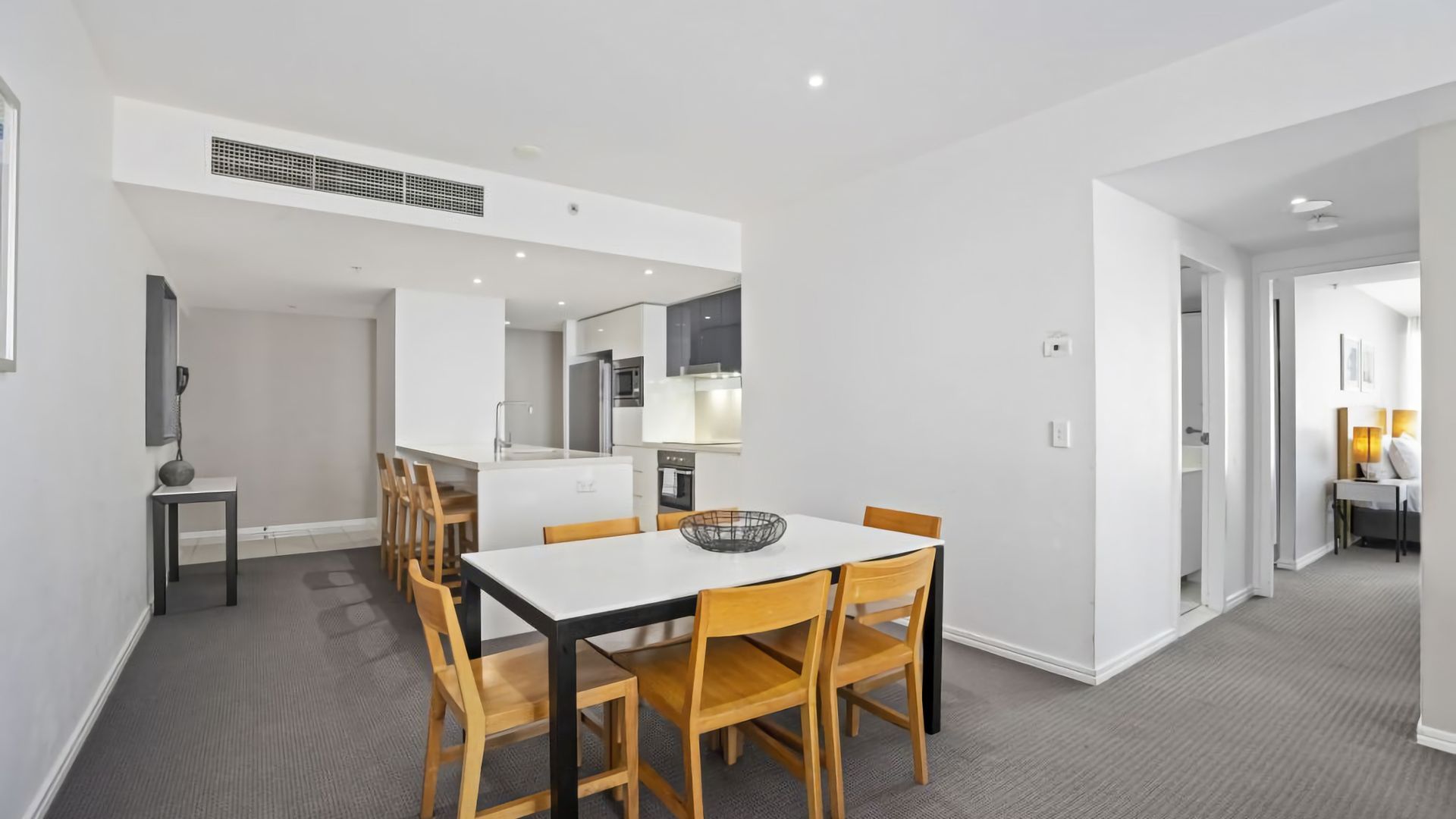 A modern kitchen with white cabinets, a central island, and a dining area with a white table and wooden chairs.