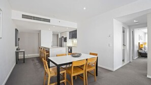 A modern kitchen with white cabinets, a central island, and a dining area with a white table and wooden chairs. - Orchid Residences Apartment 22603 (Surfers Paradise)