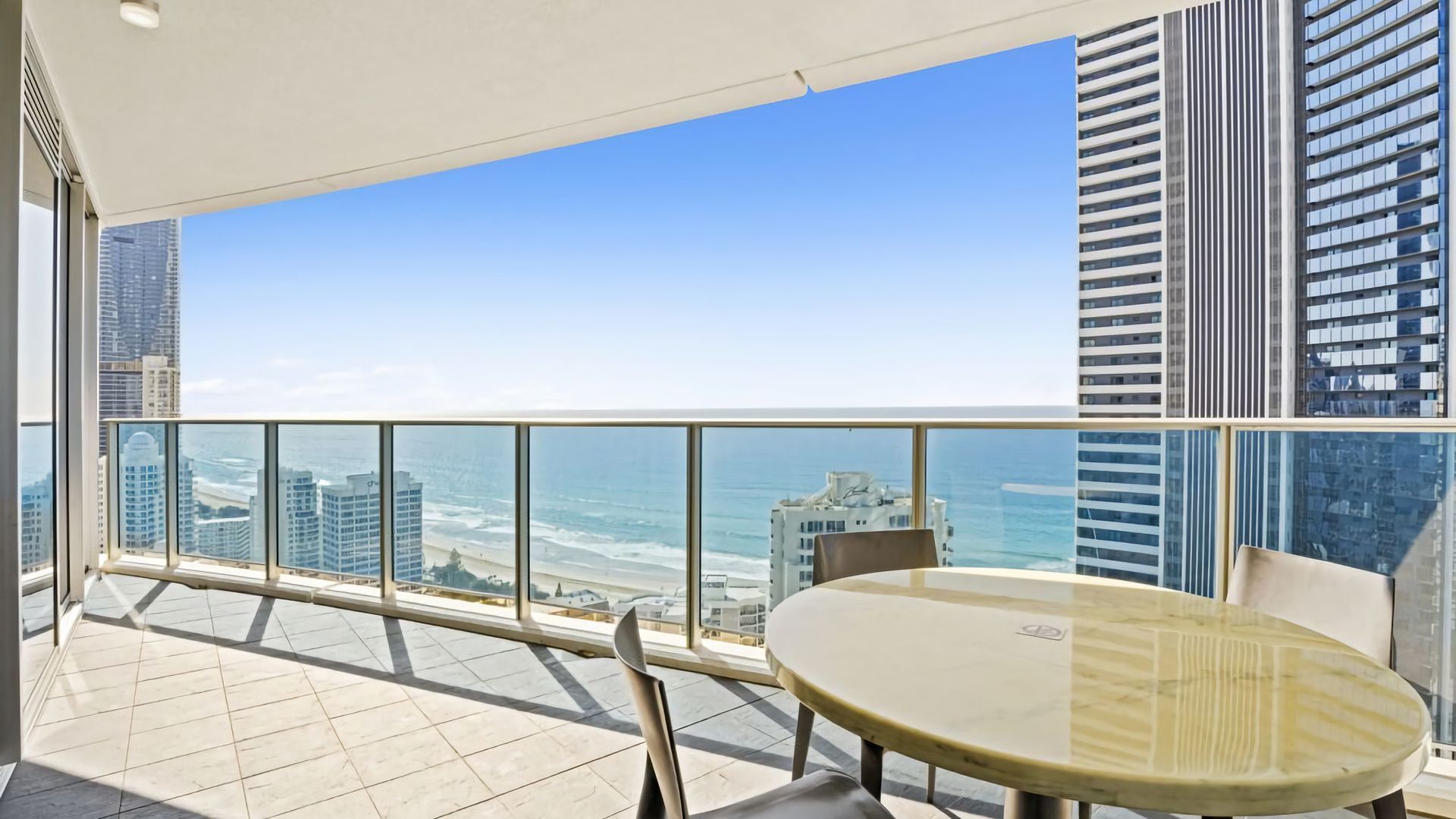 A balcony with a glass railing overlooking a beach and cityscape.