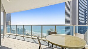 A balcony with a glass railing overlooking a beach and cityscape. - Orchid Residences Apartment 22603 (Surfers Paradise)