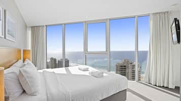 A hotel room with a large bed, a headboard, a flat-screen TV, and a view of the city and ocean.
