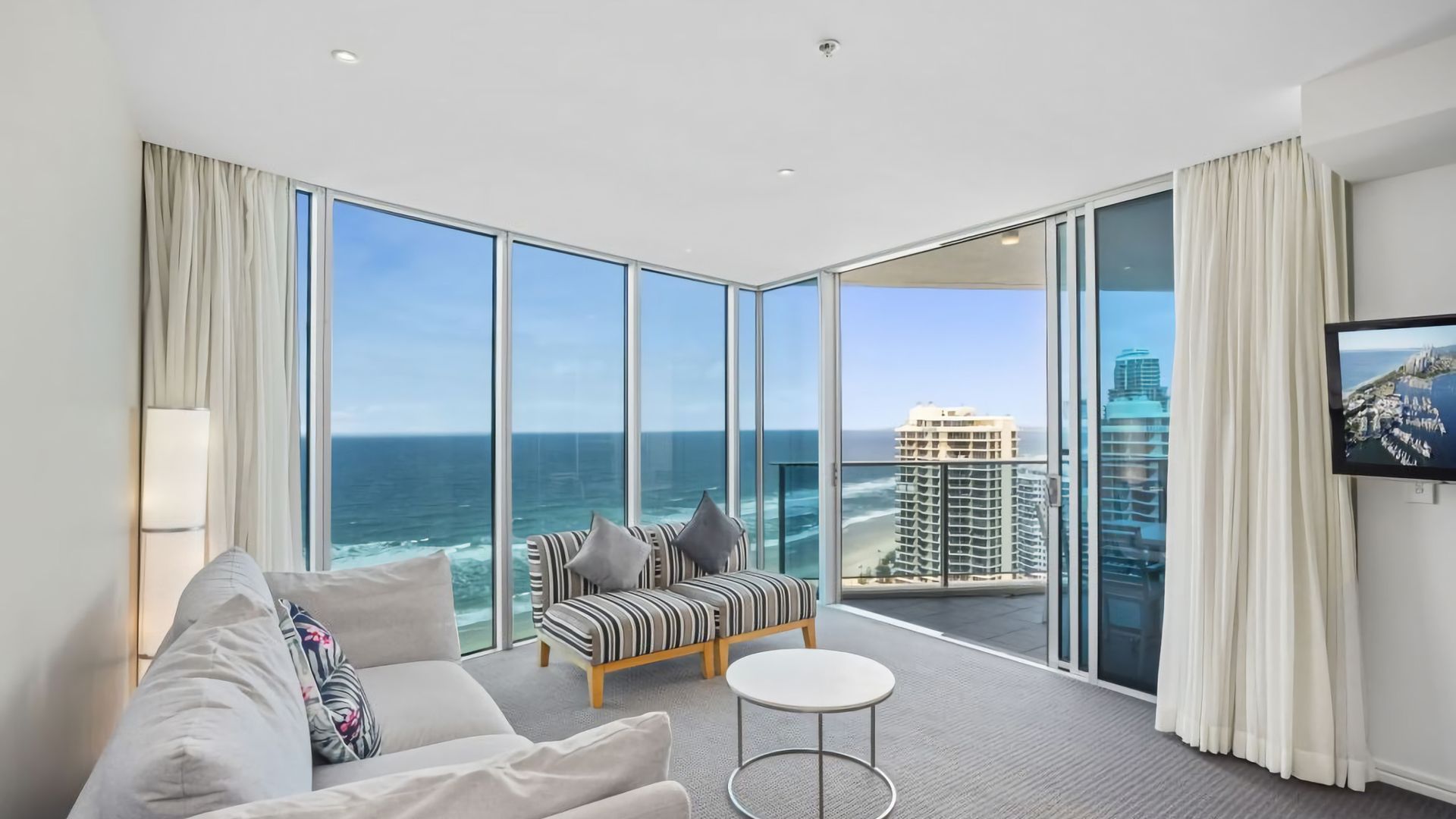 A modern hotel room with a large balcony, a sofa, a small table, and a TV.