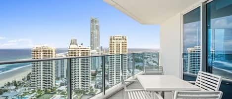 A balcony with a table and chairs overlooking a cityscape and beach.