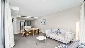 A modern living room with a white sofa, a round coffee table, and a dining area with a table and chairs. - Orchid Residences Apartment 22604 (Surfers Paradise)