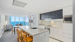 A modern kitchen with a central island, stainless steel appliances, and a view of the ocean. - Orchid Residences Apartment 22604 (Surfers Paradise)