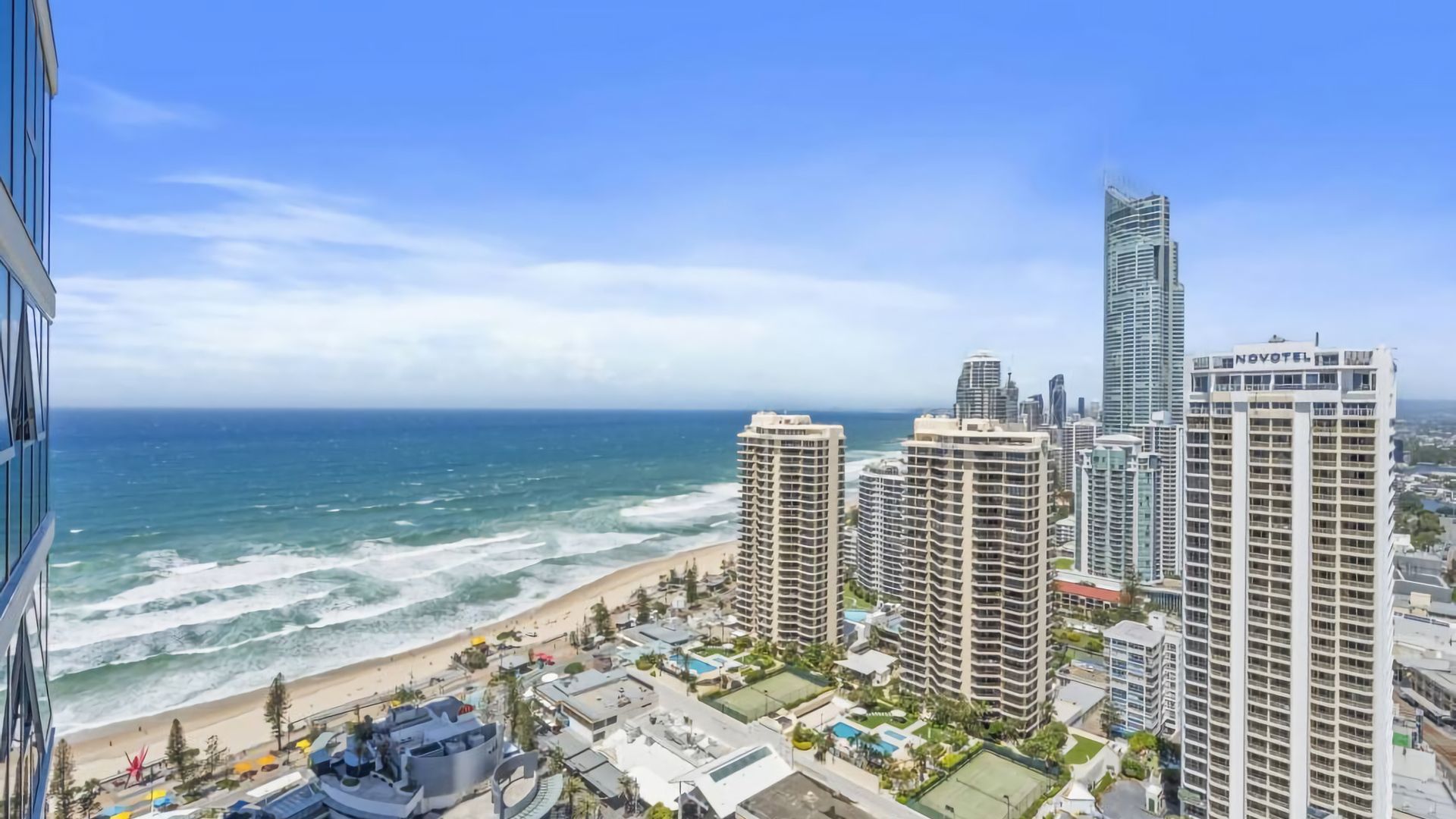 A coastal cityscape with high-rise buildings, a beach, and a clear sky.