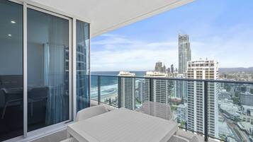 A balcony with a table and chairs, overlooking a cityscape and the ocean.