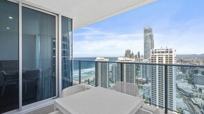A balcony with a table and chairs, overlooking a cityscape and the ocean. - Orchid Residences Apartment 22905 (Surfers Paradise)