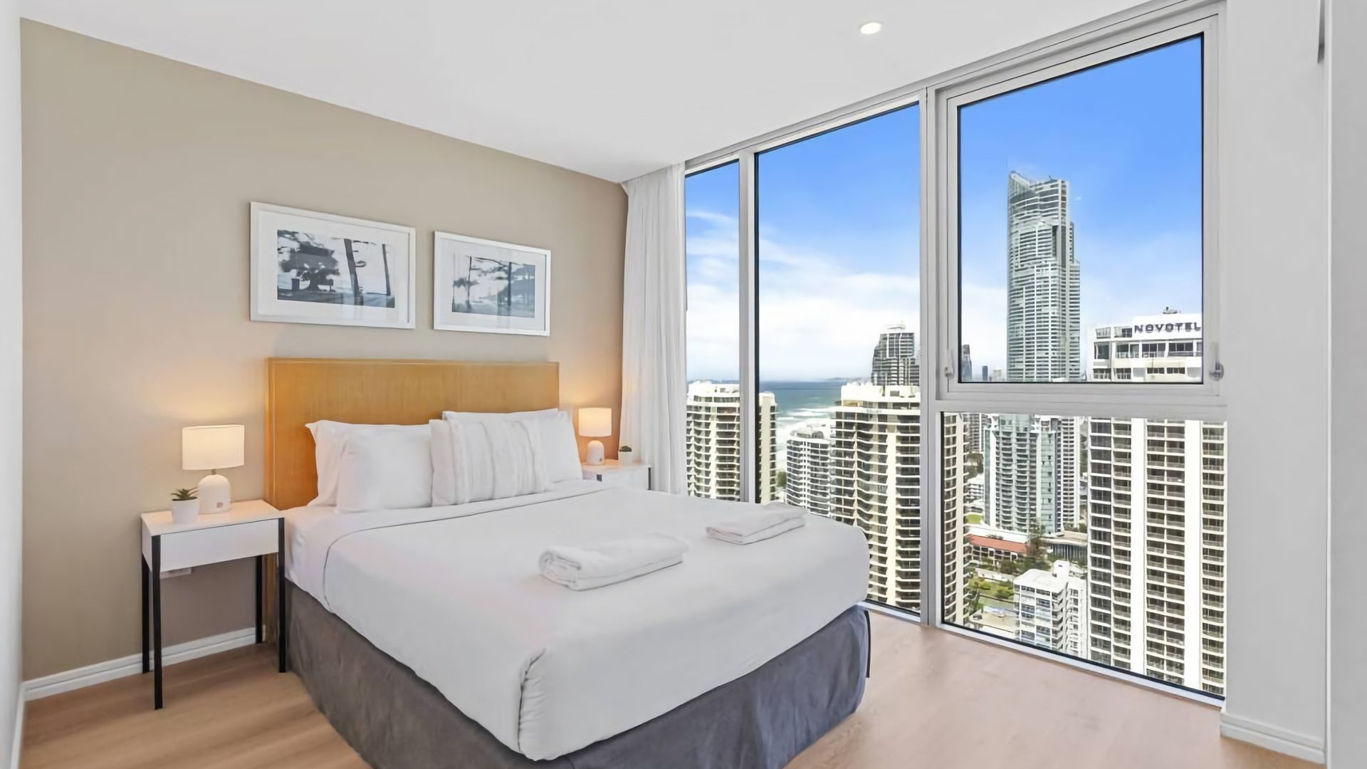 A hotel room with a large bed, a nightstand, a lamp, and a view of high-rise buildings.