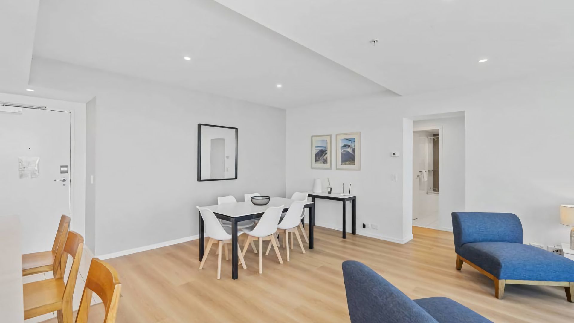 A modern living room with a dining area, a blue sofa, and a wooden chair.