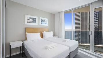 A hotel room with two beds, a large window with a view of buildings, and framed pictures on the wall.