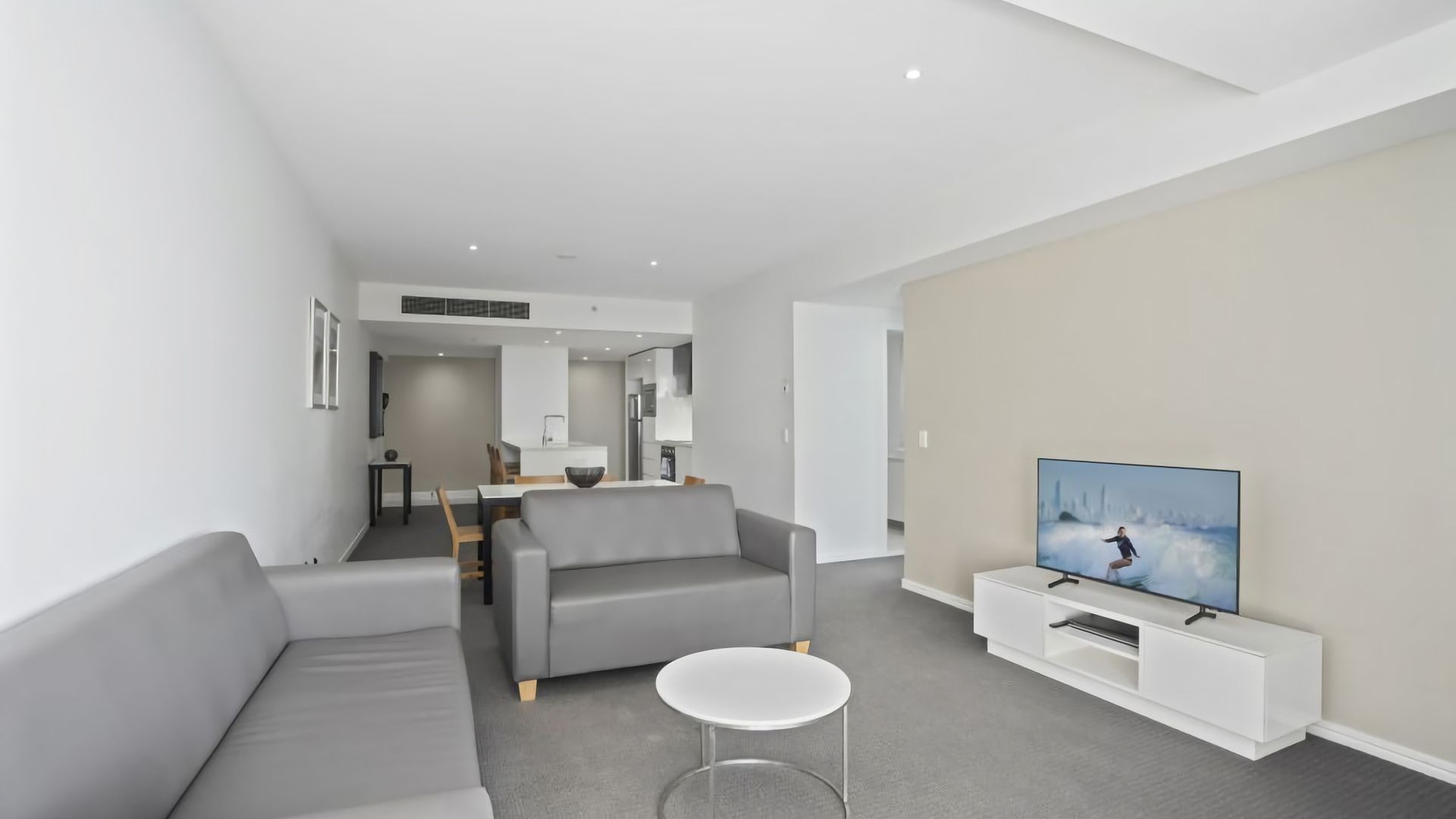A modern living room with a grey sofa, a white coffee table, and a flat-screen TV on a white stand.
