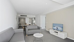 A modern living room with a grey sofa, a white coffee table, and a flat-screen TV on a white stand. - Orchid Residences Apartment 23003 (Surfers Paradise)