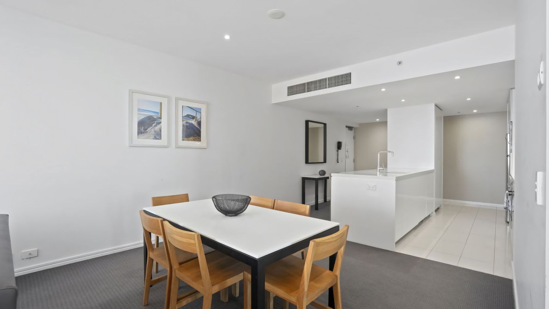 A modern kitchen with white cabinetry, a central island, and a dining area with a white table and wooden chairs.