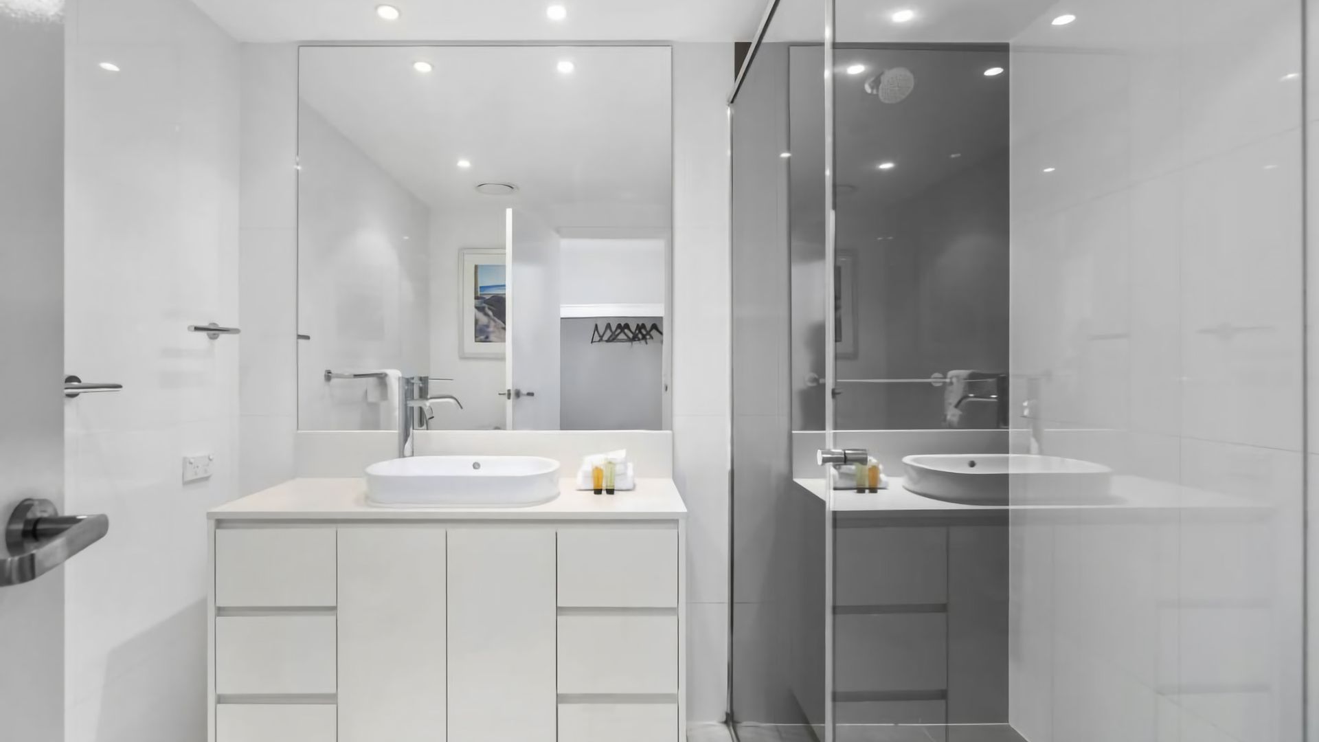 A modern bathroom with two sinks, a glass shower enclosure, and a large mirror.