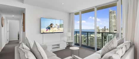 A modern hotel room with a large balcony, a flat-screen TV, and a view of the city skyline.