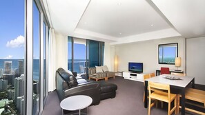 Moderni hotellihuone, josta on näkymä kaupunkiin, ja jossa on sohva, ruokapöytä ja televisio.