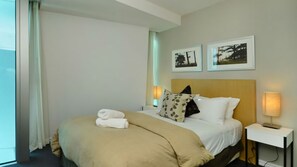 A hotel room with a bed, two bedside tables, a window with curtains, and two framed pictures on the wall. - Orchid Residences Apartment 23701 (Surfers Paradise)