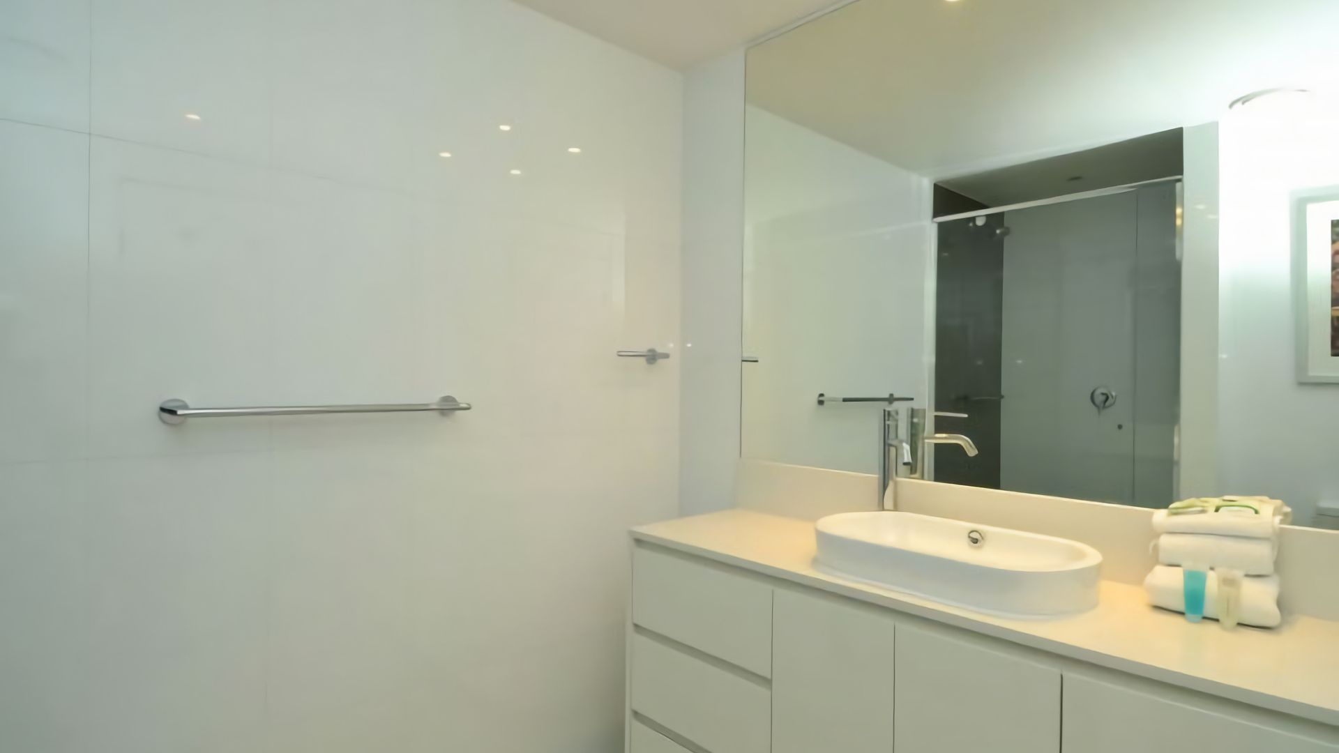 Un bagno moderno con doccia a filo pavimento, uno specchio grande e un lavandino bianco con erogatore di asciugamani.