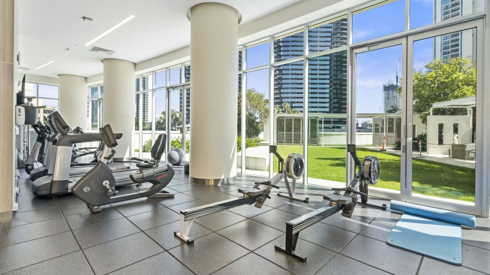 A gym with exercise equipment and large windows offering a view of the city.
