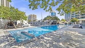A swimming pool with lounge chairs and umbrellas, surrounded by trees and modern buildings. - Orchid Residences Apartment 23802 (Surfers Paradise)