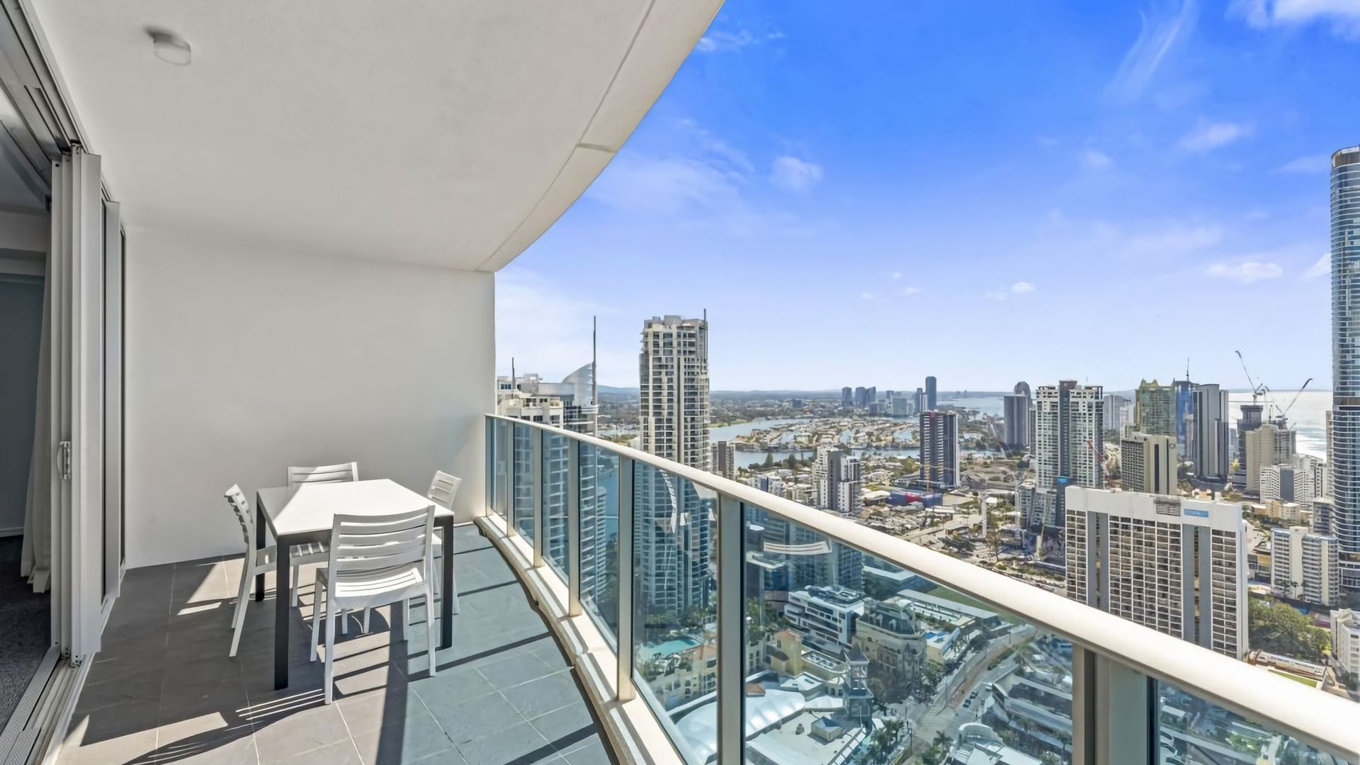 A balcony with a table and chairs, overlooking a cityscape with high-rise buildings.