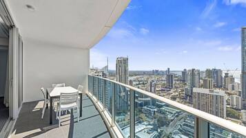 A balcony with a table and chairs, overlooking a cityscape with high-rise buildings.