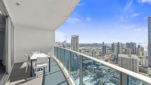 A balcony with a table and chairs, overlooking a cityscape with high-rise buildings. - Orchid Residences Apartment 23802 (Surfers Paradise)