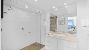 A modern bathroom with a glass-enclosed shower, a large mirror, and a vanity with a sink. - Orchid Residences Apartment 23802 (Surfers Paradise)