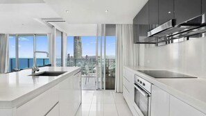 A modern kitchen with a large island, stainless steel appliances, and a view of the cityscape. - Orchid Residences Apartment 23805 (Surfers Paradise)