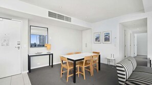 A modern living room with a dining area, a sofa, and a view of the city. - Orchid Residences Apartment 23805 (Surfers Paradise)