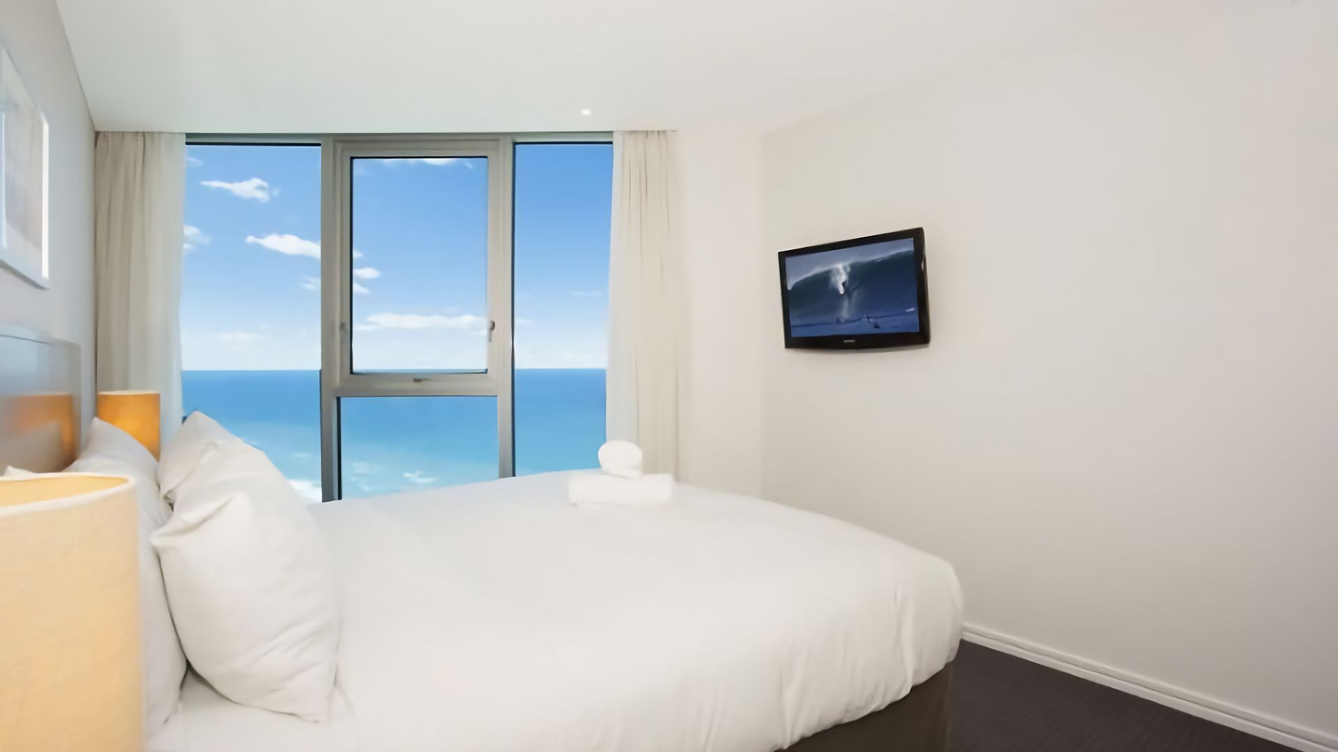 A hotel room with a bed, a television, and a view of the ocean.