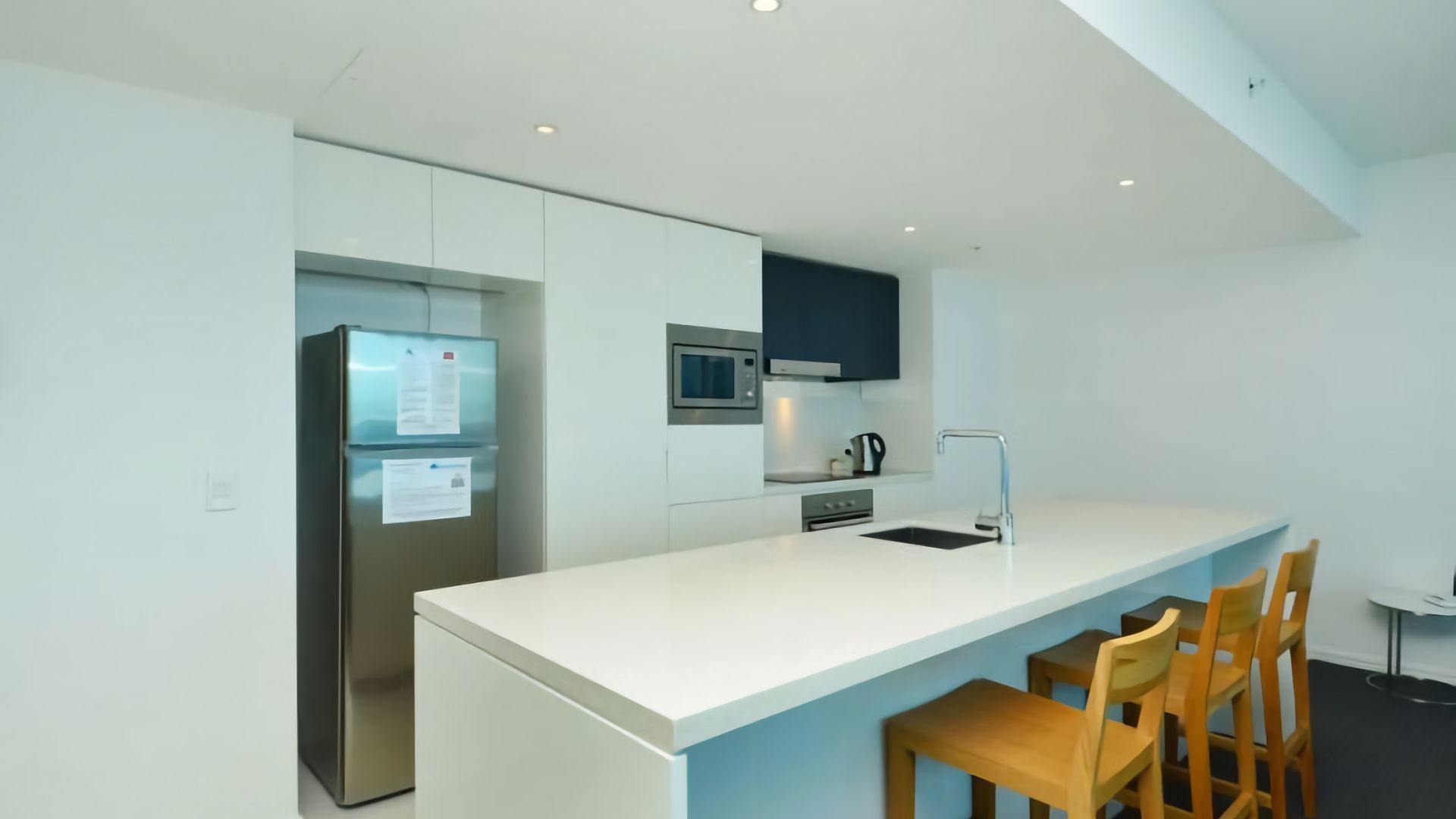 A modern kitchen with a white countertop, stainless steel appliances, and wooden chairs.