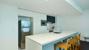 A modern kitchen with a white countertop, stainless steel appliances, and wooden chairs.