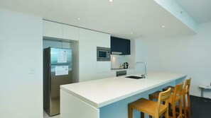A modern kitchen with a white countertop, stainless steel appliances, and wooden chairs. - Orchid Residences Apartment 24402 (Surfers Paradise)