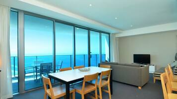 A modern hotel room with a balcony, a dining area, a sofa, and a television.
