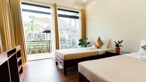 Habitación de hotel con balcón, dos camas, cómoda de madera y plantas en macetas.