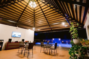 An indoor space with a high ceiling, a television mounted on the wall, a dining area with chairs and a table, and a water feature in the background. - Asian vanda Villa  (Puerto Princesa City)
