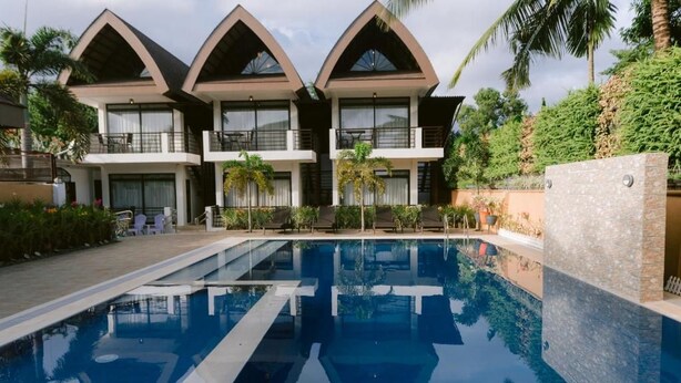 Un hotel moderno con piscina, varios balcones y exuberante vegetación.
