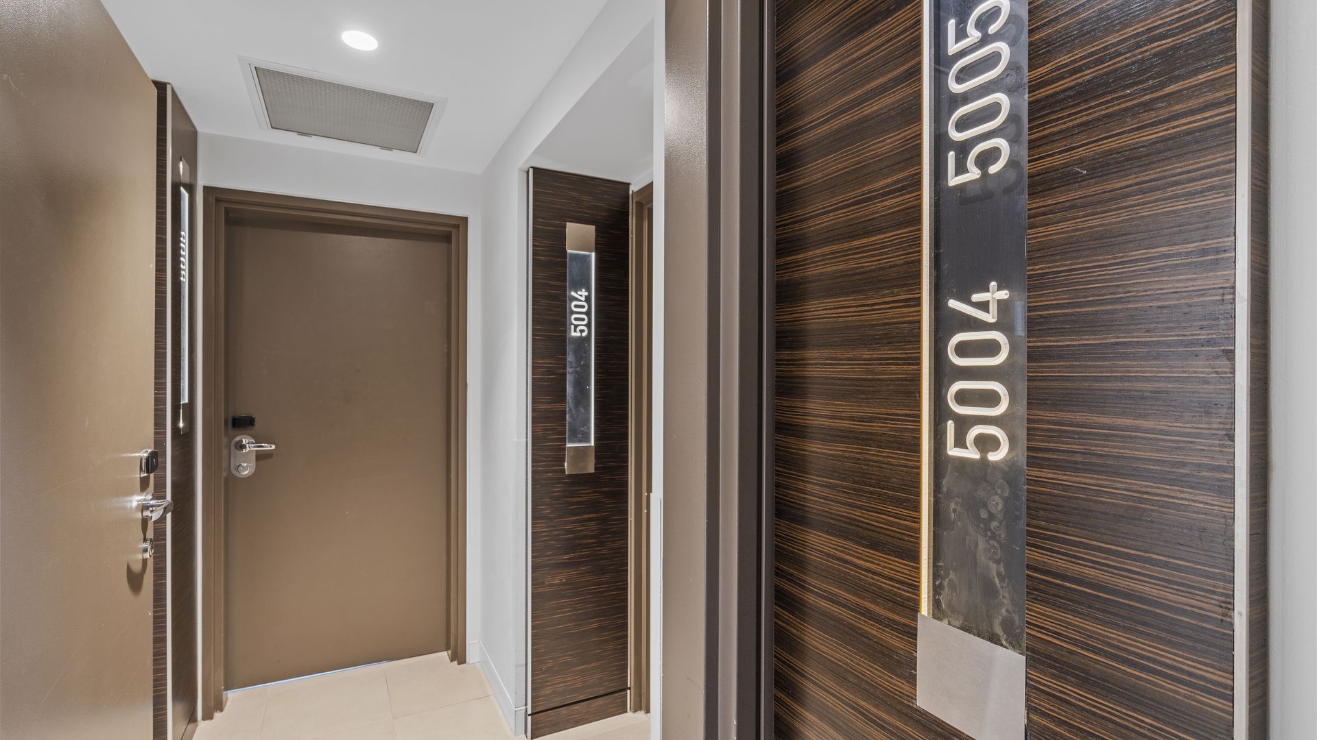 A hallway with a closed door, a wall-mounted sign with numbers, and a wooden textured wall.