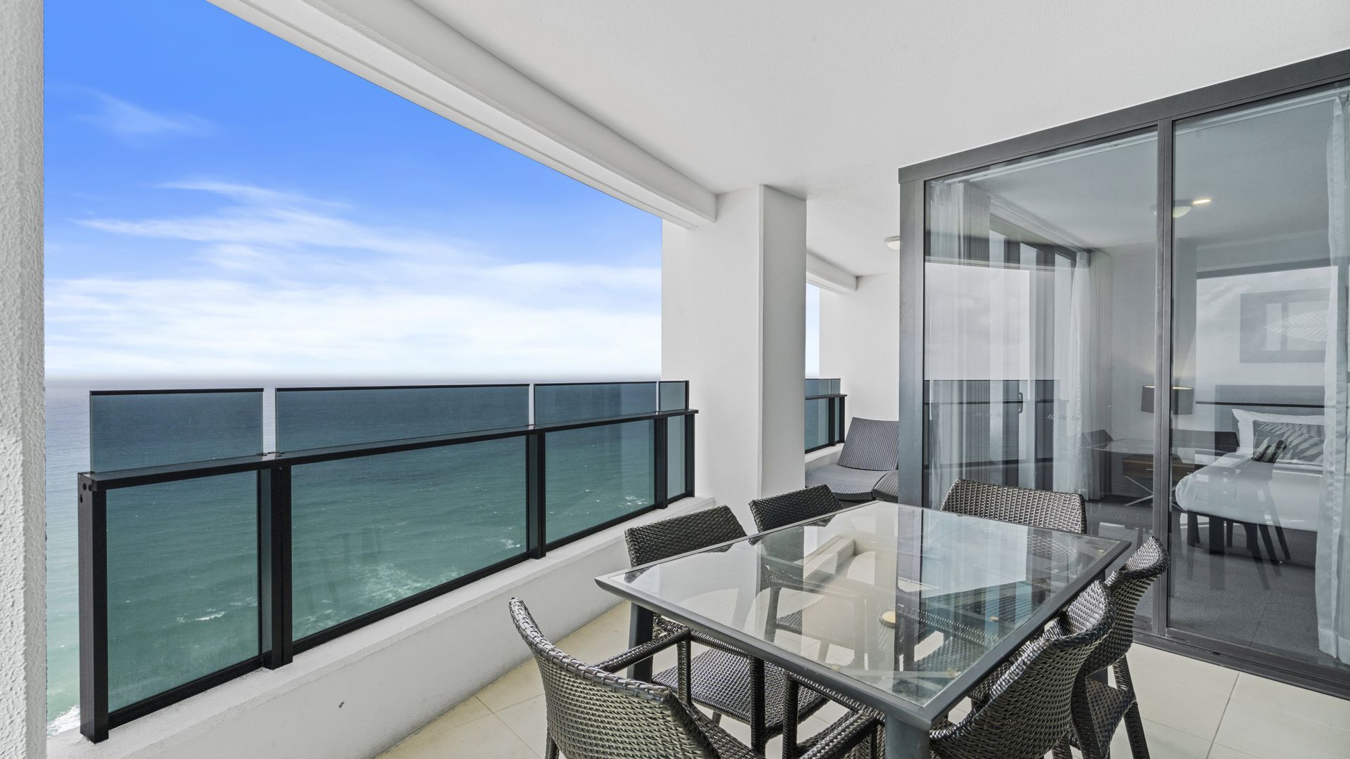 Ein Balkon mit Glastisch und Stühlen, mit Blick auf das Meer.